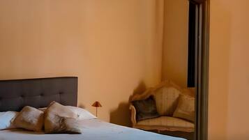 Un dormitorio con cama, almohadas, una silla y una mesita de noche.