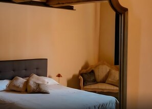Een slaapkamer met een bed, kussens, een stoel en een nachtkastje.