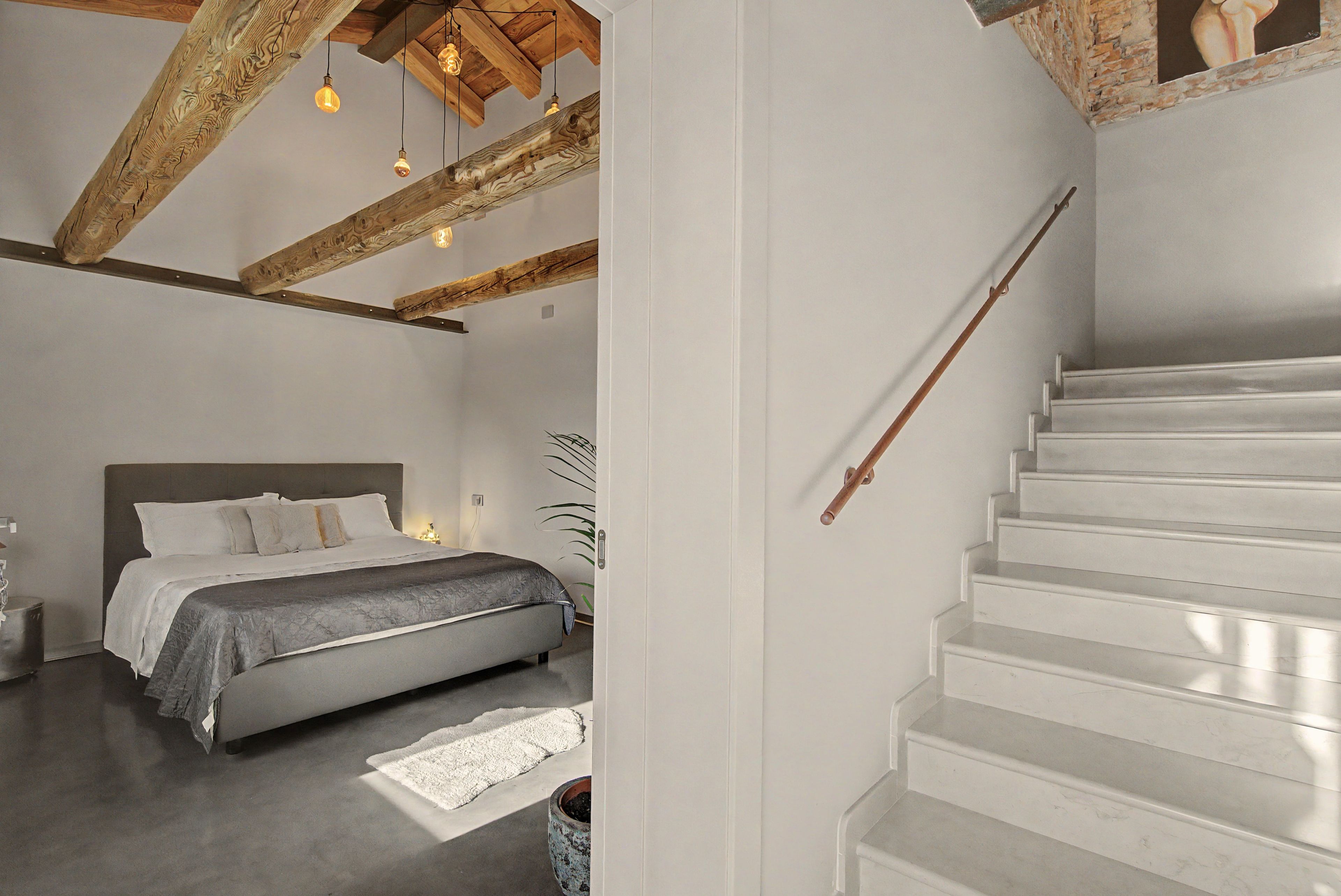 Een slaapkamer met een bed, nachtkastje en een trap.