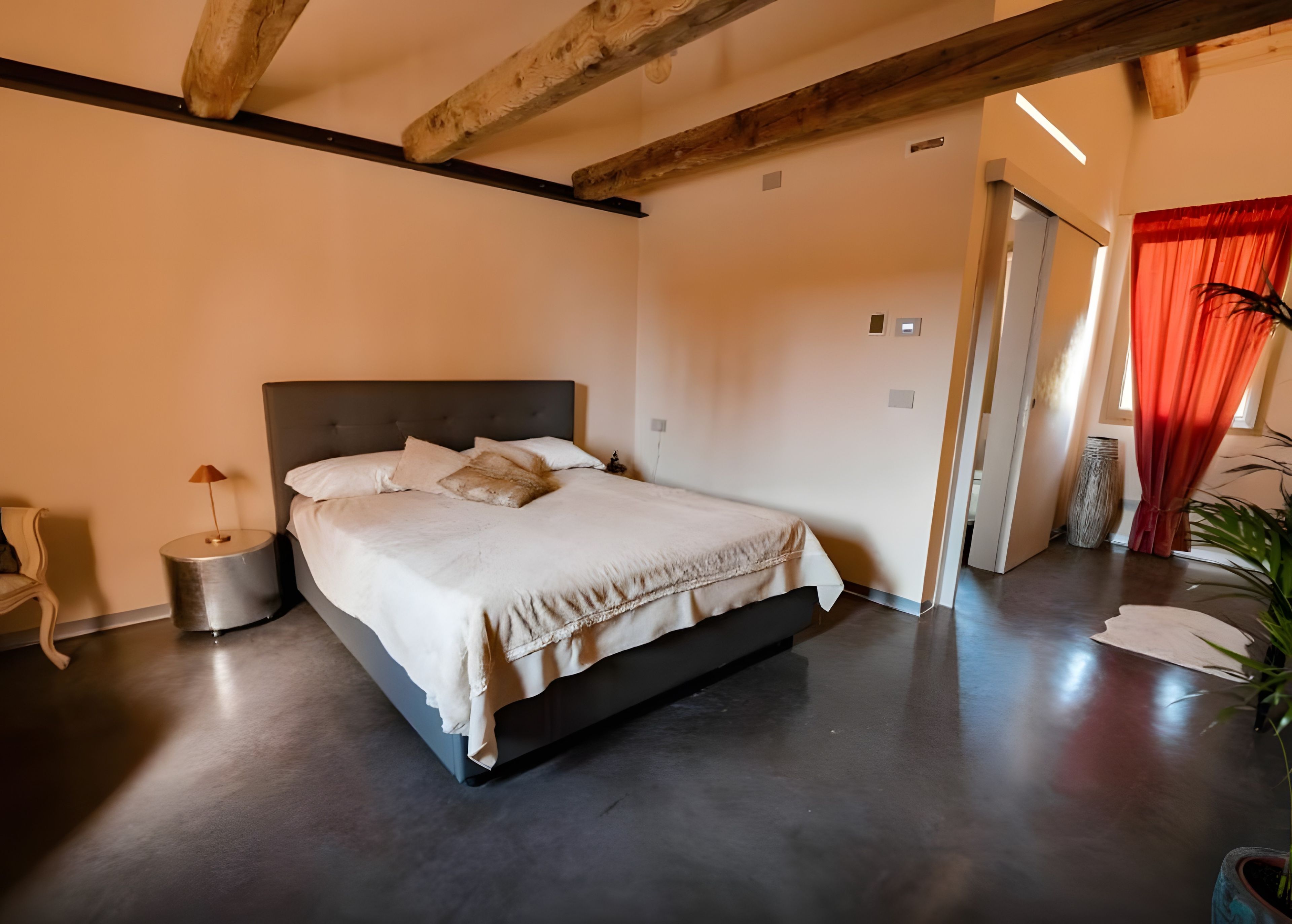 Een moderne slaapkamer met een groot bed, een bedlampje en een kamerplant.