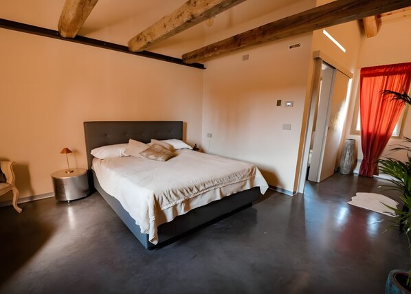 Een moderne slaapkamer met een groot bed, een bedlampje en een kamerplant.