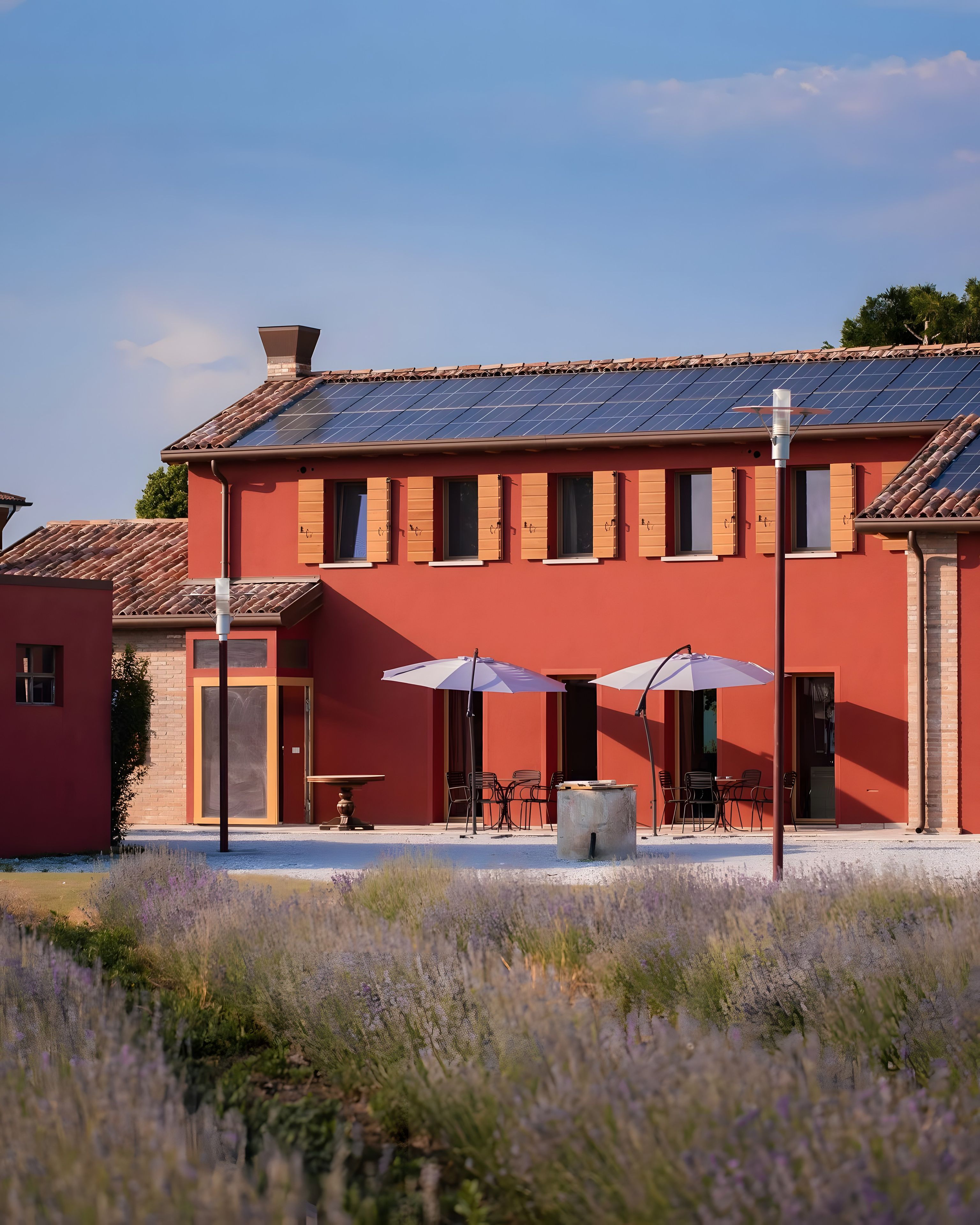 Een rood gebouw met pannendak, zonnepanelen en terras met parasols.