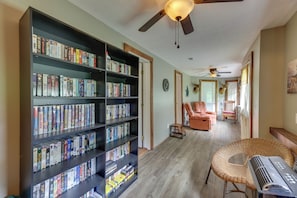 A room with a large bookshelf filled with books, a ceiling fan, a wicker chair, and a small table.