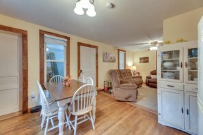 A dining area with a wooden table and white chairs, a living room with a brown sofa and a cabinet with glass doors, and a ceiling fan. - Rural WV Escape w/ Hilltop Mountain Views (Tallmansville)