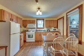 A kitchen with wooden cabinets, a refrigerator, a stove, a microwave, and a dining table with chairs.