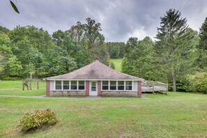 A small, single-story building with a brick facade and large windows, surrounded by a grassy field and dense trees. - Rural WV Escape w/ Hilltop Mountain Views (Tallmansville)