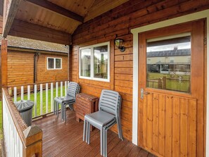 A wooden deck with a white railing, two grey plastic chairs, and a small table. - Log Cabin One - UK51959 (Sutton-on-Sea)