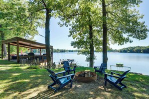 A lakeside outdoor seating area with a covered picnic table, chairs, and a fire pit. - Log Home on Tipsico Lake w/ Beach & Dock (Holly)