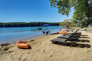 A lakeside beach with lounge chairs, a paddle boat, and a canopy. - Log Home on Tipsico Lake w/ Beach & Dock (Holly)