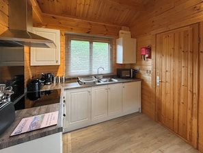A compact kitchen with wooden cabinets, a sink, a microwave, and a stove. - Log Cabin Three - UK51961 (Sutton-on-Sea)