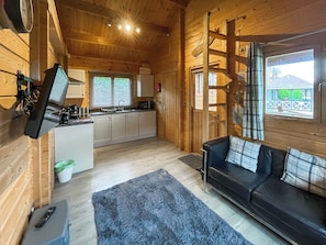 A cozy cabin interior with a kitchen, a sofa, and a TV. - Log Cabin Three - UK51961 (Sutton-on-Sea)