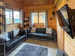 A cozy cabin interior with a black leather sofa, a grey rug, and a television mounted on the wall. - Log Cabin Five - UK51963 (Sutton-on-Sea)