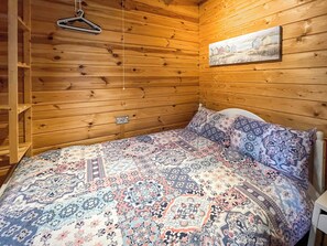 Ett rum med träpanel på väggarna, en säng, en klädstång och en inramad tavla på väggen.