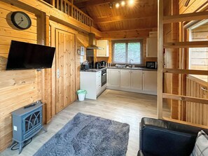 A wooden interior with a kitchen, a television mounted on the wall, and a small rug on the floor. - Log Cabin Four - UK51962 (Sutton-on-Sea)