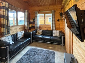A cozy living room with a black leather sofa set, a grey fluffy rug, and a flat-screen TV mounted on the wall. - Log Cabin Four - UK51962 (Sutton-on-Sea)