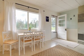 A room with a white table and chairs, a window with curtains, a door with a handle, and a radiator.