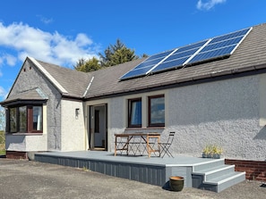Ein Haus mit geneigtem Dach, Solaranlage, überdachter Veranda und Backsteinfundament.