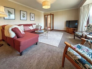A living room with a red sofa, a glass coffee table, a television, and a floral-patterned chair. - Roanbank - The Hidden Road Retreat (Castle Douglas)