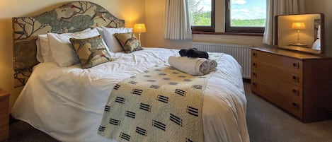 Una cama bien hecha con un edredón estampado, un cabecero con diseño floral y un aparador con espejo.