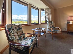 A room with two floral-patterned chairs, a small table with a chess set, and a view of a landscape through large windows. - Roanbank - The Hidden Road Retreat (Castle Douglas)