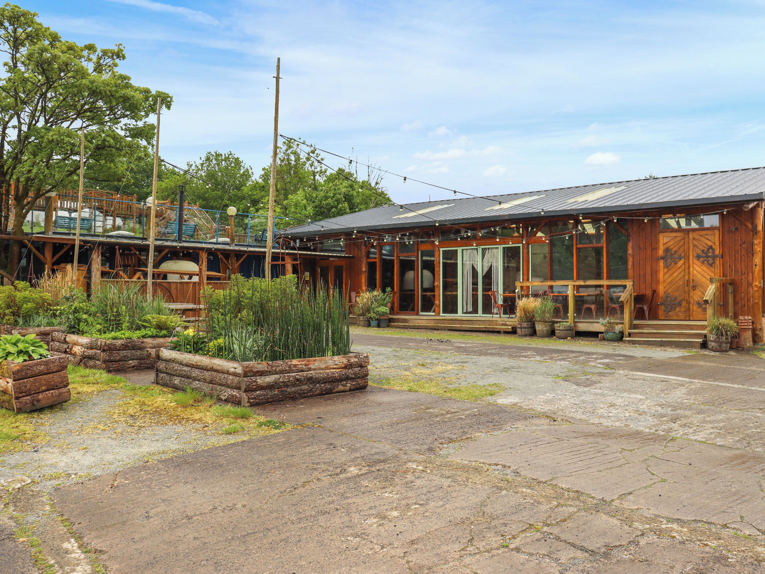 A rustic wooden building with a porch, large windows, and a garden area with raised beds.