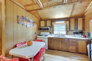 A cabin-style kitchen with wooden walls, a dining table with red chairs, a stove, and a sink. - Fish the Right Fork River: Tallmansville Home (Tallmansville)