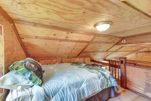 A wooden cabin bedroom with a bed, a headboard, and a slanted ceiling. - Fish the Right Fork River: Tallmansville Home (Tallmansville)