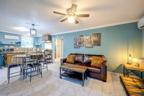 A living room with a brown leather couch, a dining table with chairs, a kitchen area, and a ceiling fan. - On-Site Trails & Wildlife! Hill Country Escape (Utopia)