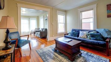 A living room with hardwood flooring, a blue sofa with patterned cushions, a wooden coffee table, and a lamp.