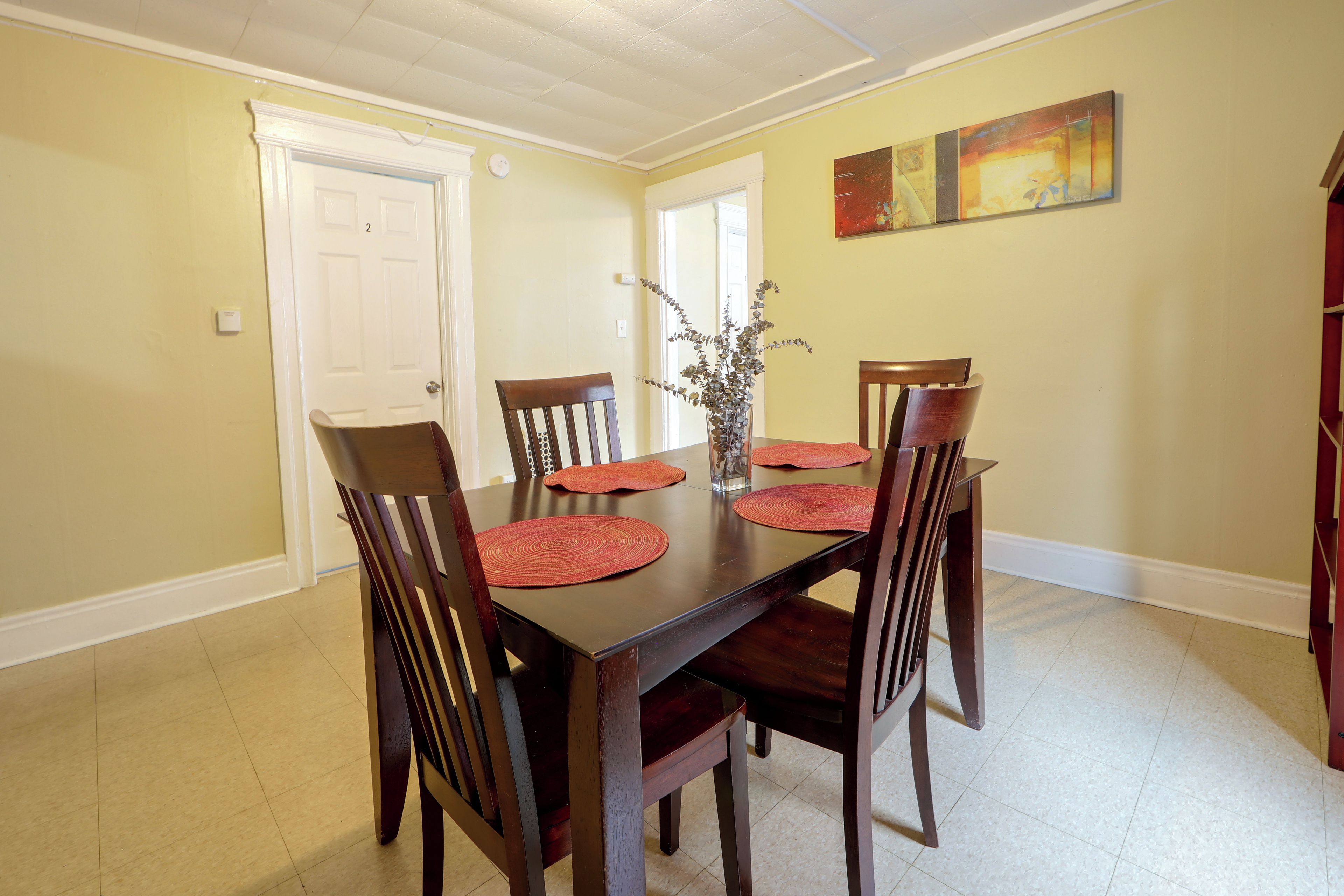 A dining room with a wooden table, six chairs, and a vase with dried flowers.