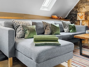 A grey sectional sofa with patterned and solid green cushions, a wooden coffee table, and a stone wall with a fireplace. - Hen Stabal - UK51984 (Llanfair, near Harlech)