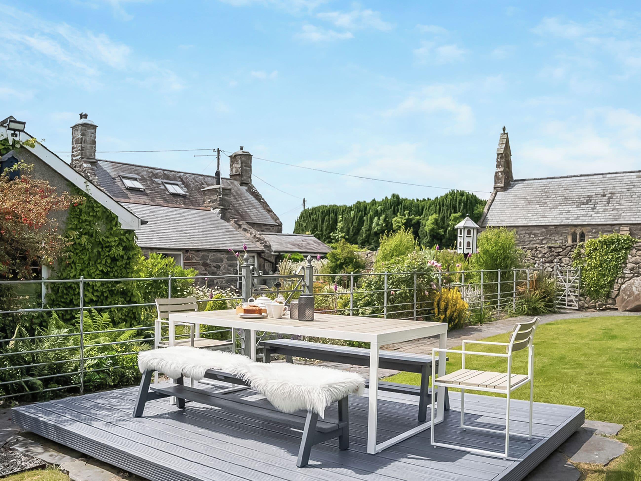 A patio with a table and benches, surrounded by a stone wall and greenery.