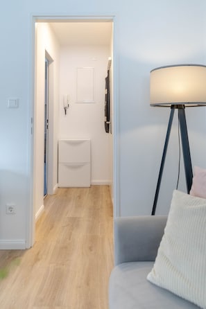 A room with a grey sofa, a floor lamp, and a view into a bathroom with a white sink and towel rack. - Marien4 - Möve1 - Prime Location - Right on the Beach (Sylt)