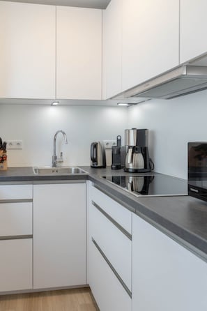A modern kitchen with white cabinets, a stainless steel sink, and two coffee makers. - Marien4 - Möve1 - Prime Location - Right on the Beach (Sylt)
