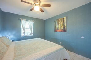 A bedroom with a bed, a ceiling fan, a window with curtains, and a painting on the wall. - Lazy Oak Cabins: Rustic Hill Country Cabin (Utopia)