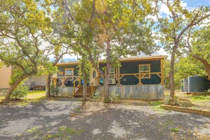 A rustic cabin with a wooden deck and a large window, surrounded by trees. - Lazy Oak Cabins: Rustic Hill Country Cabin (Utopia)