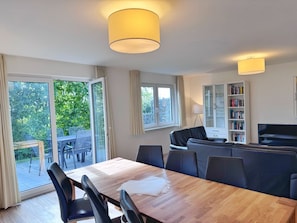 A modern living room with a dining area, a sofa, a bookshelf, and a television. - Modern three-bedroom semi-detached home with a fireplace - Mein Glowe - DHH Links (Glowe)