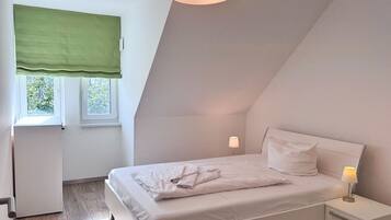 A bedroom with a bed, bedside tables, a window with a green blind, and a ceiling light.