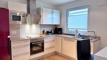 A compact kitchen with a microwave, oven, and a window with blinds.