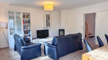 A modern living room with a sofa set, a flat-screen TV, and a bookshelf.