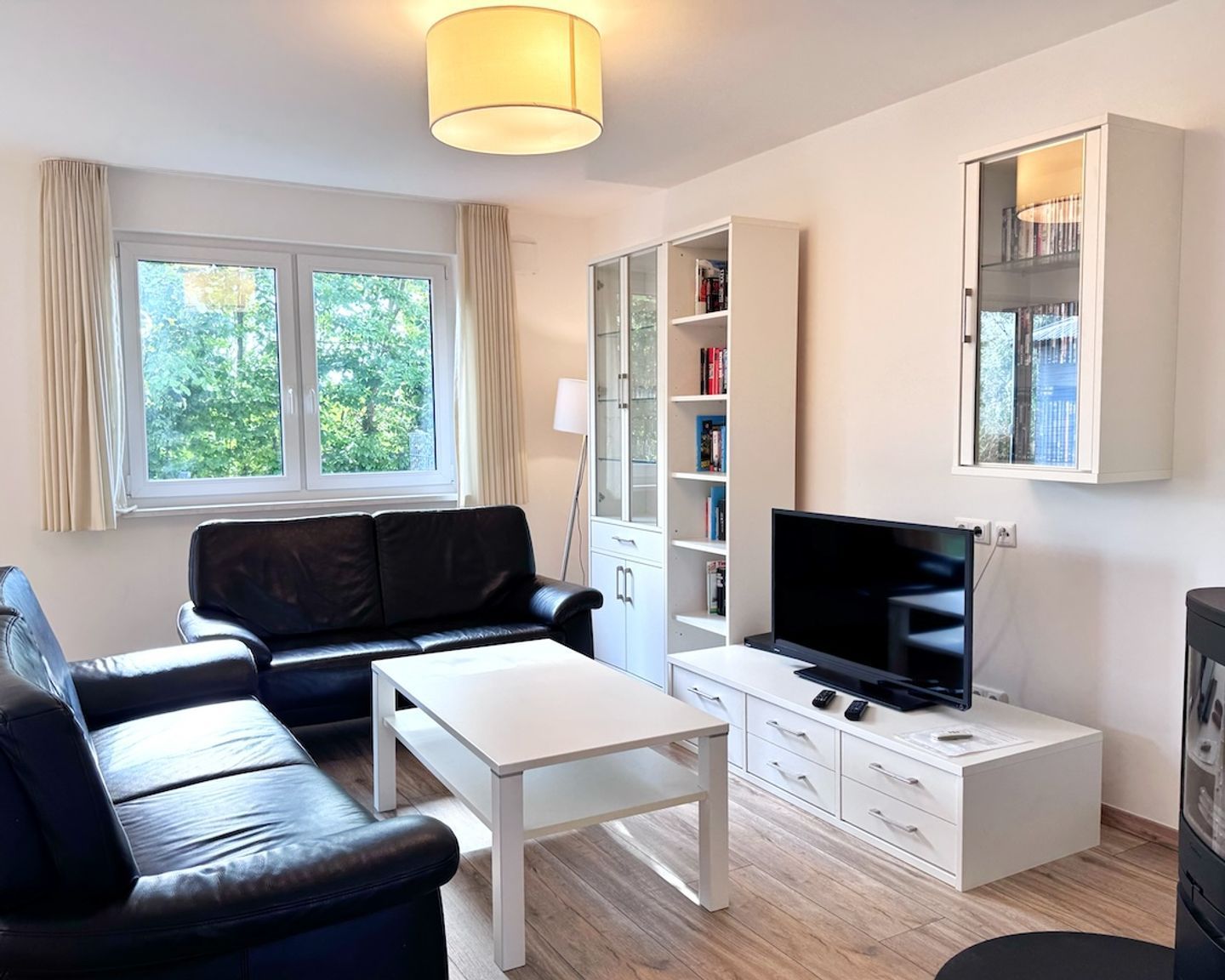 A modern living room with a black leather sofa, a white coffee table, a flat-screen TV, a bookshelf, and a cabinet.