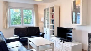 A modern living room with a black leather sofa, a white coffee table, a flat-screen TV, a bookshelf, and a cabinet.