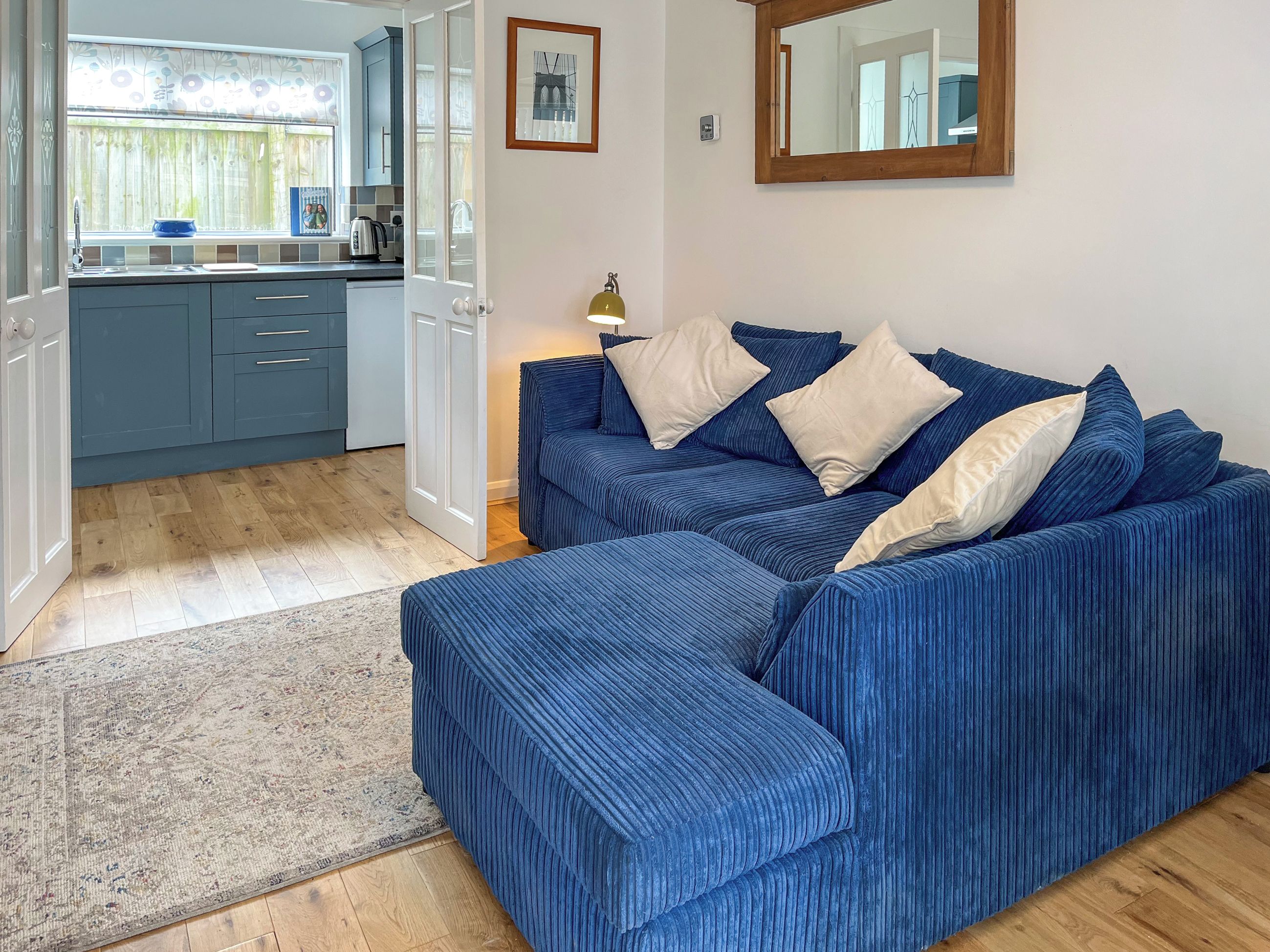 A room with a blue sofa, a rug, a kitchen area, and a mirror on the wall.