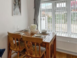A dining table set with plates, glasses, and a vase of flowers, positioned near a window with blinds. - 2 bedroom accommodation in Killham (Killham)