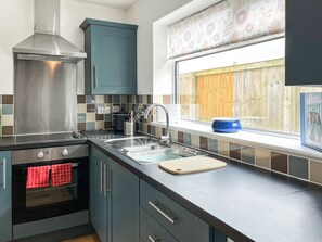 Ett modernt kök med rostfria vitvaror, ett fönster med utsikt över ett trästaket och en bok som står på fönsterbrädan.