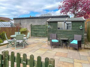 A wooden cottage with a tiled patio, two wicker chairs with cushions, and a small table. - 2 bedroom accommodation in Killham (Killham)