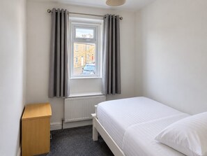 Une chambre avec un lit simple, un radiateur, une fenêtre avec des rideaux et une armoire en bois.