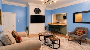 A living room with a sofa, a coffee table, a TV, and a kitchen area with a bar. - Beautiful & Cosy Newly Renovated House in Blaydon (Blaydon)