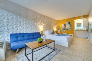 Ein modernes Wohnzimmer mit einem blauen Sofa, einem Holztisch und einem weißen Bett mit blauer Decke.