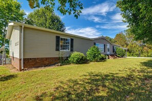 A single-story house with a brick foundation, a flat roof, and a front yard with grass and shrubs. - 22-Acre Farm Retreat < 8 Mi to Kentucky Lake! (Dexter)